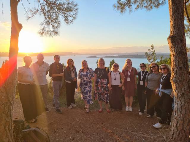 Grupo de personas sonriendo frente a un paisaje con atardecer sobre el agua.
