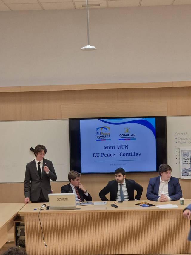 Un grupo de personas asisten a un evento académico con una presentación sobre temas de paz en la EU en Comillas.