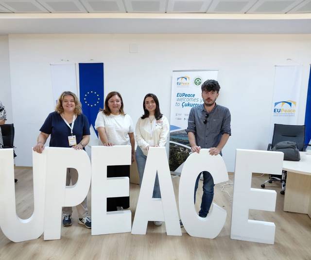 Un grupo de personas sostiene letras grandes que forman la palabra 'UPEACE' en un entorno de conferencia.
