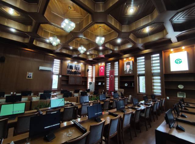 La imagen muestra un salón de conferencias bien iluminado con computadoras y decoraciones en madera.