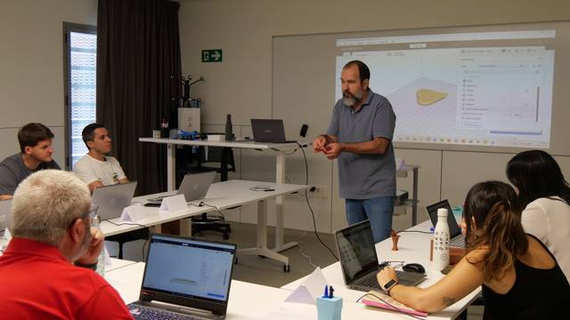 Un grupo de personas asiste a una clase práctica mientras un instructor presenta información en una pantalla.