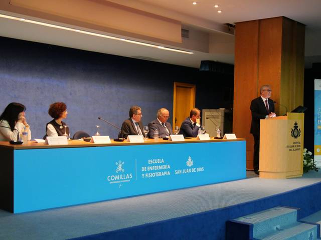 Un evento académico con varias personas en una mesa y un presentador frente a un público.