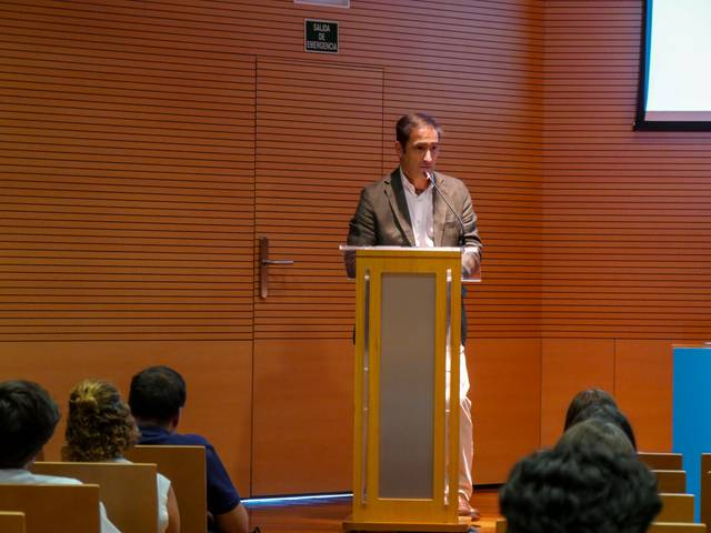 Un orador se encuentra frente a un público en una sala de conferencias.