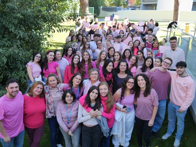 Un grupo numeroso de personas celebra un evento, todas vestidas con camisetas rosas, en un ambiente al aire libre.