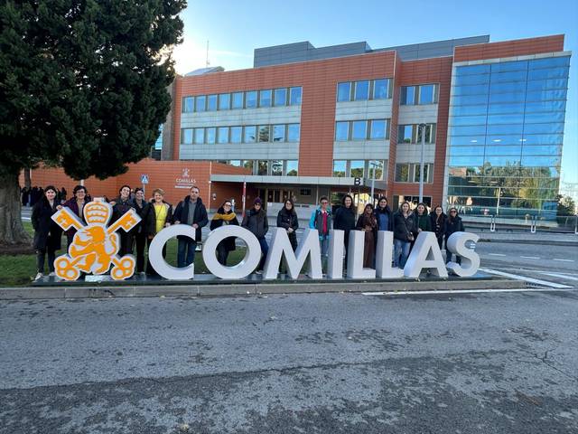 Grupo de personas posando frente al letrero que dice 'COMILLAS'.