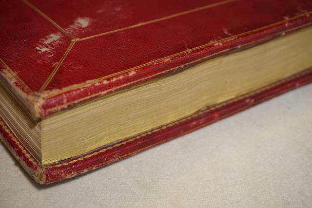 Un libro encuadernado en rojo con bordes dorados.