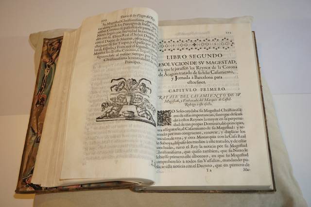 Un libro antiguo abierto muestra páginas con texto impreso y un grabado distintivo.