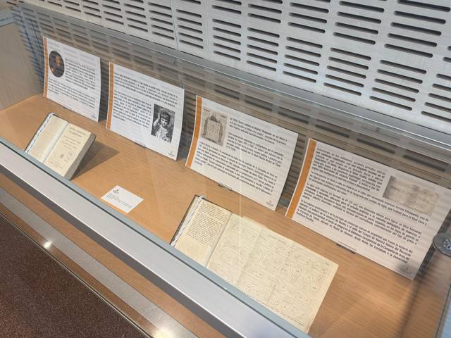La imagen muestra una vitrina con libros antiguos y paneles informativos sobre temas diversos.