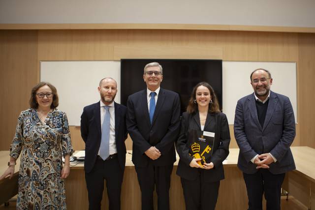 Cinco personas posan juntas en un evento formal, mostrando un premio en el centro.