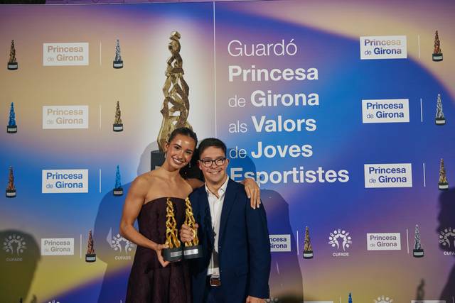 Dos personas posan sonrientes sosteniendo un premio en un evento oficial.