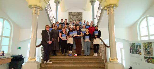 Un grupo diverso de personas posando en una escalera sostenido diplomas o certificados.