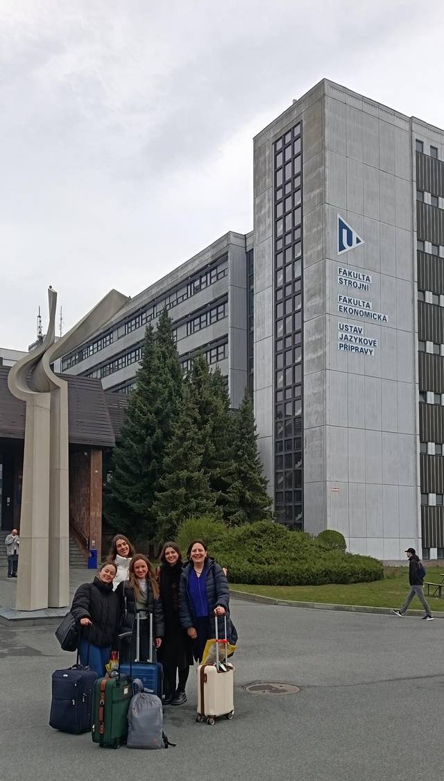 Un grupo de cinco personas posa sonriente frente a un edificio moderno de una universidad.
