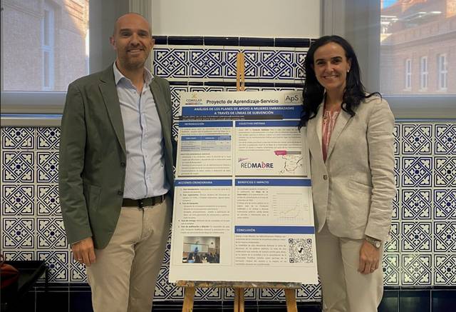 Dos personas posan junto a un cartel que presenta un proyecto de aprendizaje servicio.