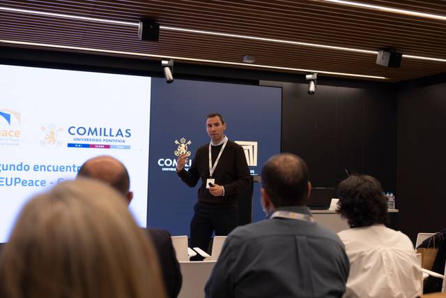 Un presentador expone en un evento frente a un público atento en una sala moderna.