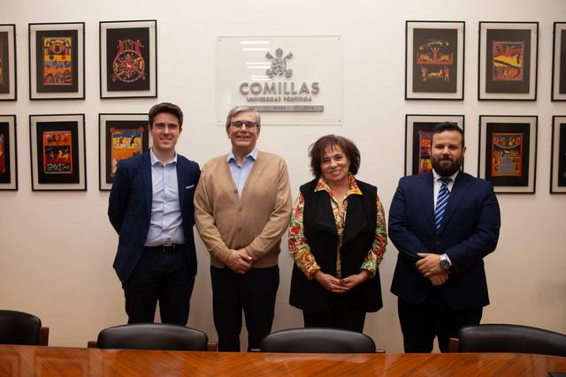 Cuatro personas posan sonrientes en un salón con un cartel de 'Comillas' y cuadros coloridos en la pared.