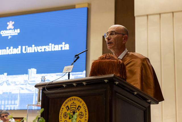 Un hombre vestido con toga y birrete está hablando en un evento académico frente a una audiencia.