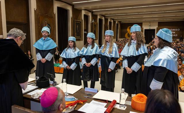 Ceremonia de graduación con estudiantes vestidos con togas y birretes en un auditorio lleno de público.