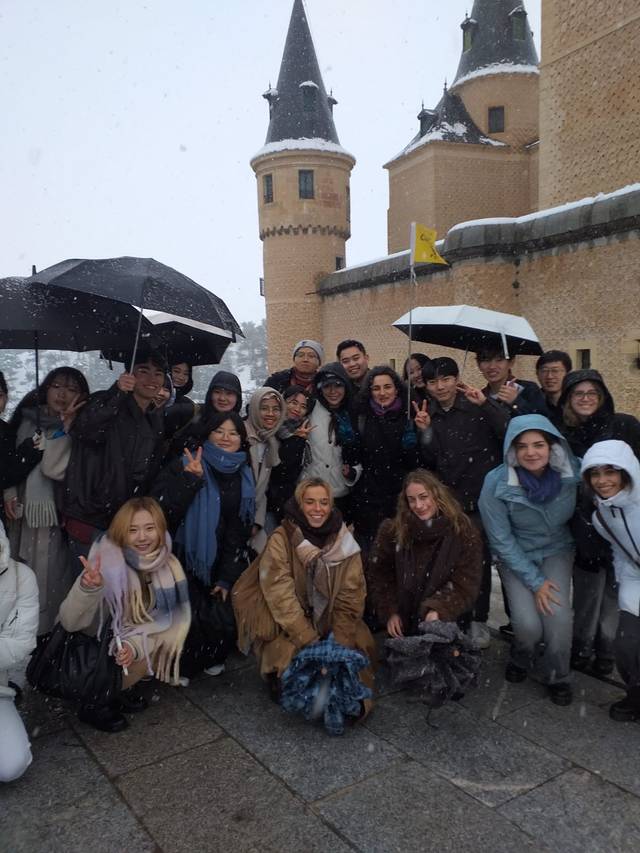 Un grupo de personas sonrientes se reúne frente a un castillo bajo la nieve.