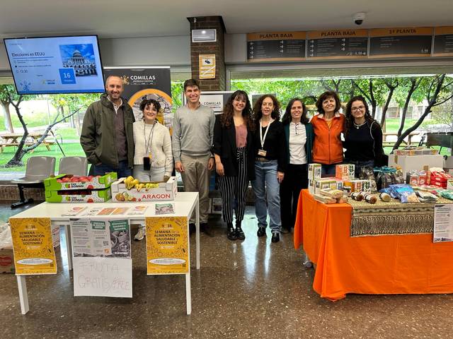 A group of people standing behind a table displaying various food items at an indoor event.