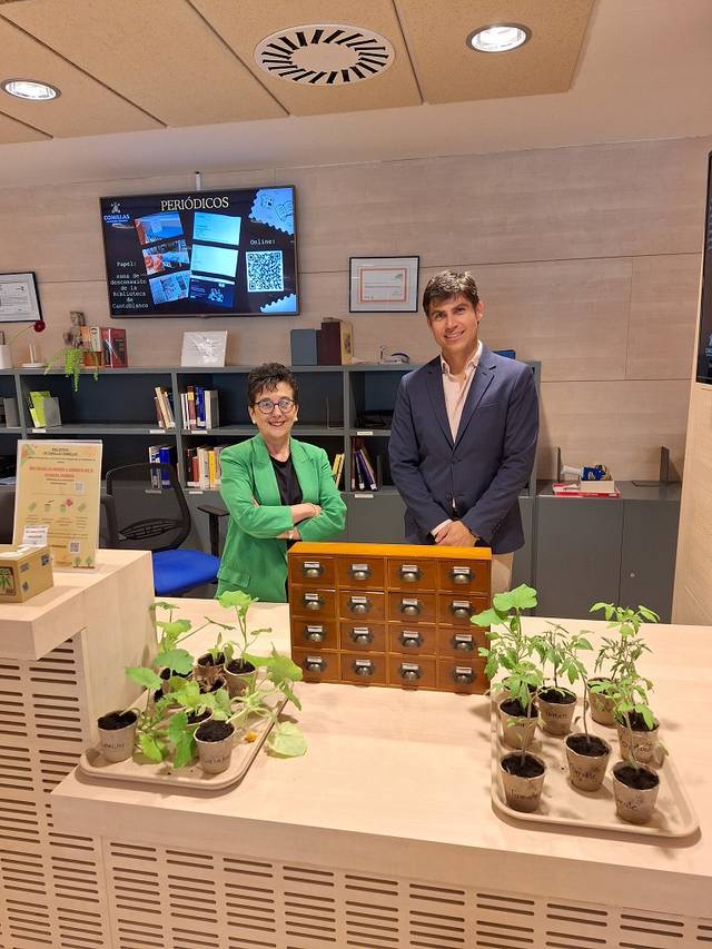 Una mujer y un hombre posan frente a un mueble con plantas en macetas y un sistema de almacenamiento en una biblioteca moderna.