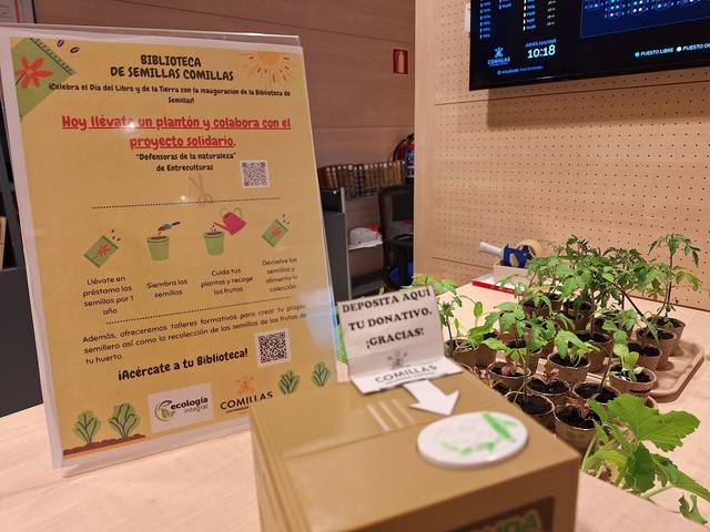 Una biblioteca de semillas en una mesa con información sobre un proyecto solidario y plantas pequeñas.
