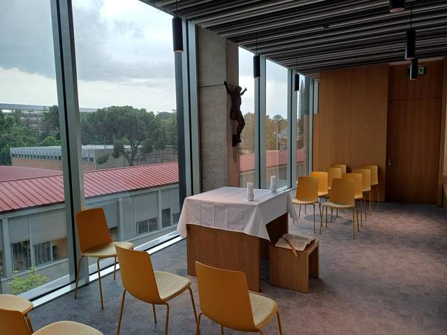 Una sala con ventanas amplias, sillas amarillas y una mesa con mantel blanco.