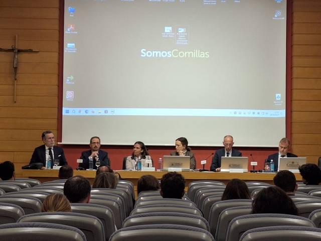 Un panel de cinco personas está sentado en frente de una audiencia en un auditorio durante un evento académico.