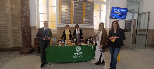 A group of people standing at a booth displaying books and pamphlets with Oxfam Intermon signage at an indoor event.