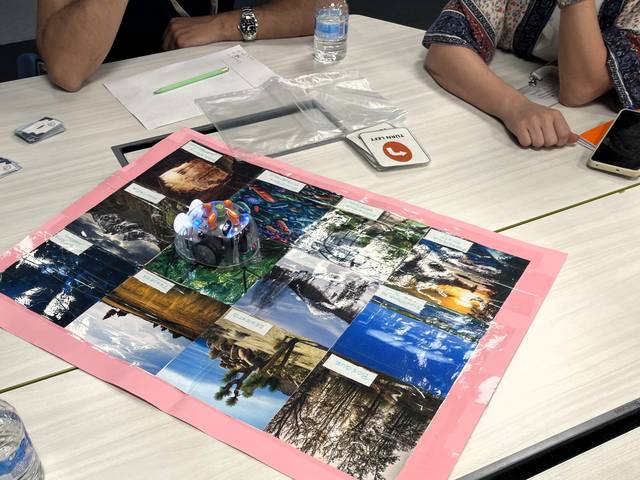 Una mesa con un collage de fotografías de paisajes y un recipiente con bolígrafos de colores en el centro.