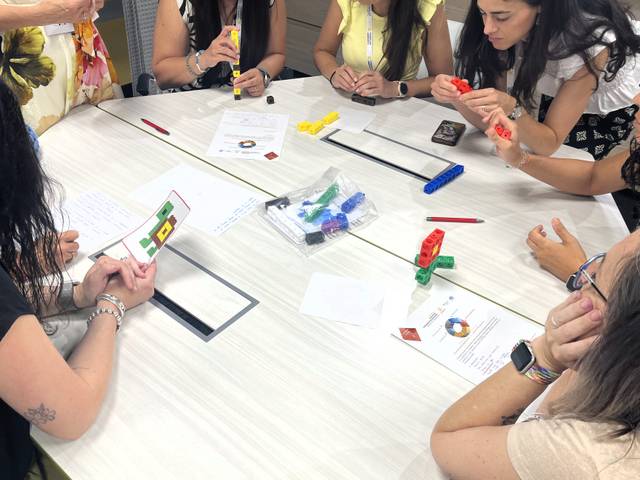 Un grupo de personas está trabajando juntas en una mesa, utilizando bloques de colores y papeles.