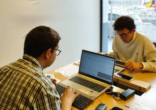 Dos jóvenes trabajando en sus computadoras portátiles en una mesa.