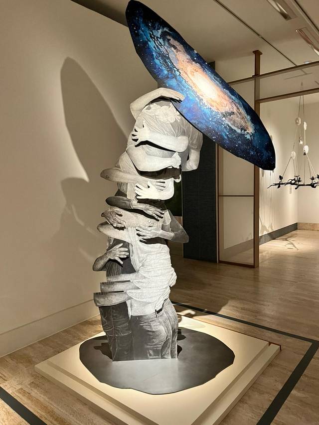Una escultura abstracta que representa una figura humanoide sosteniendo un disco que simula ser una galaxia.