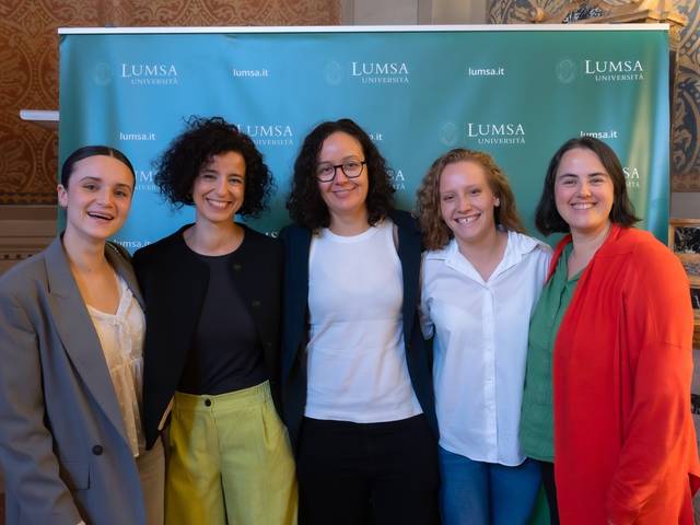 Cinco mujeres sonriendo para una fotografía frente a un banner de LUMSA University.