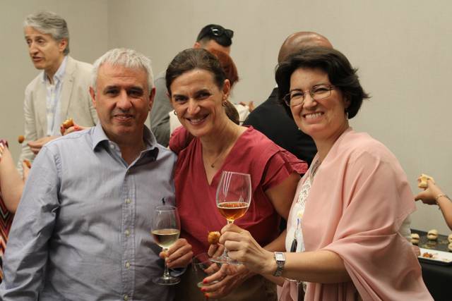 Three people smiling and holding drinks at a social gathering.