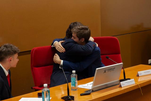 Dos hombres se abrazan en una sala de conferencias ante un público.