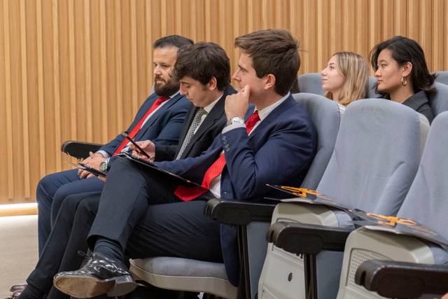 Un grupo de personas sentadas en un evento formal, prestando atención y tomando notas.