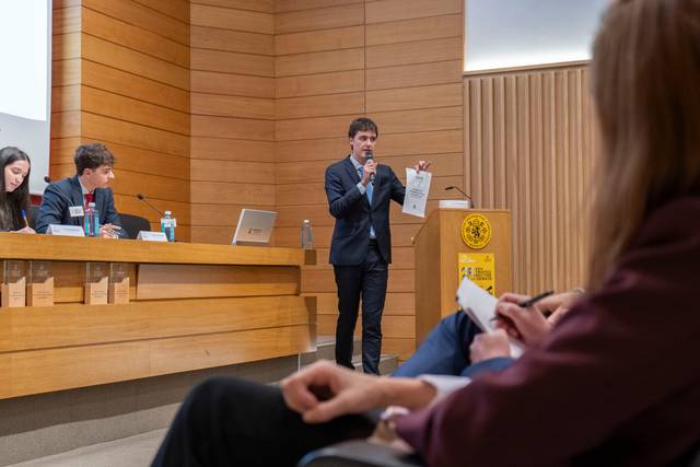 Un joven presenta un documento mientras está de pie frente a una audiencia en un evento académico.
