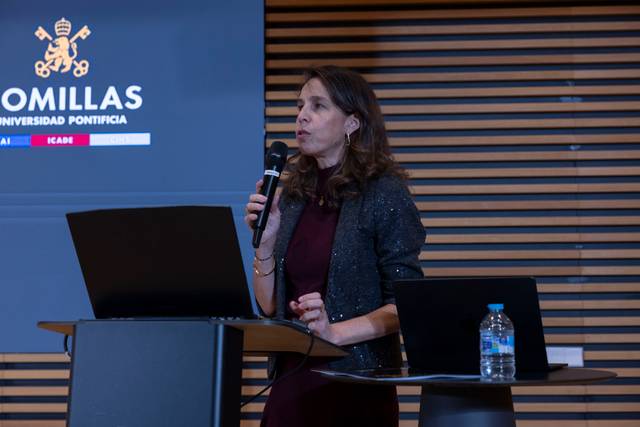 Una mujer está dando una presentación en un evento académico con un ordenador portátil frente a ella.