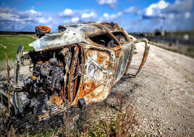 Un automóvil quemado y oxidado está abandonado al borde de un camino rural.
