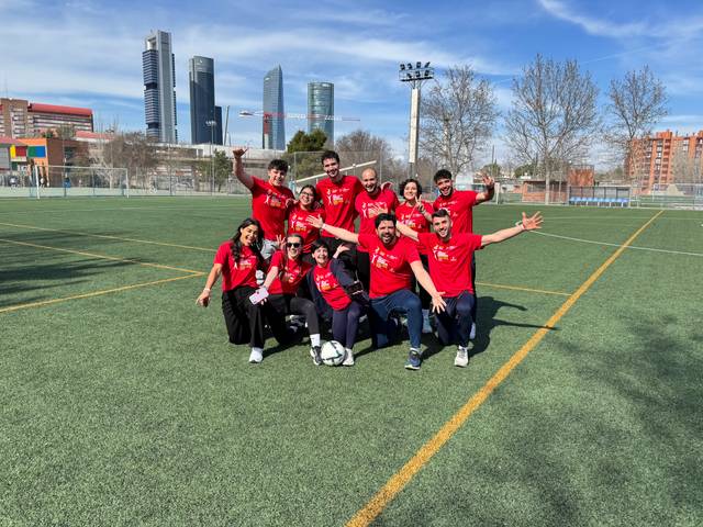 Grupo de personas en un campo de fútbol, todos vestidos con camisetas rojas y sonriendo.