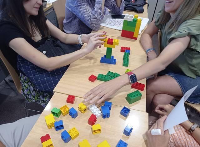 People sitting around a table playing and building with colorful toy blocks.