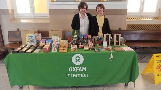 Two women standing behind a table covered with various products at an Oxfam Intermón promotional event.