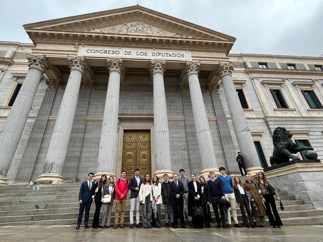 Un grupo de personas posa frente al Congreso de los Diputados en un día nublado.