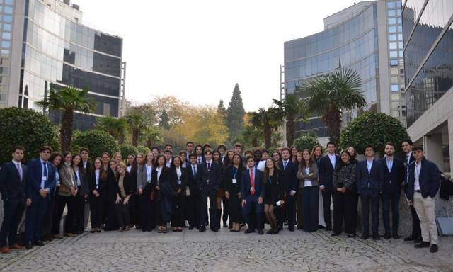 Un grupo de personas vestidas de manera formal se encuentra en un camino empedrado entre edificios de oficinas.