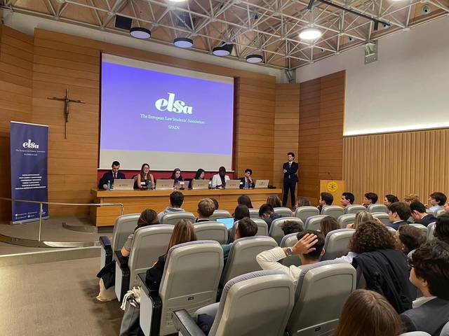 Personas asistiendo a una conferencia en un auditorio con un panel de ponentes en el estrado y un logotipo de 'elsa' en el fondo.