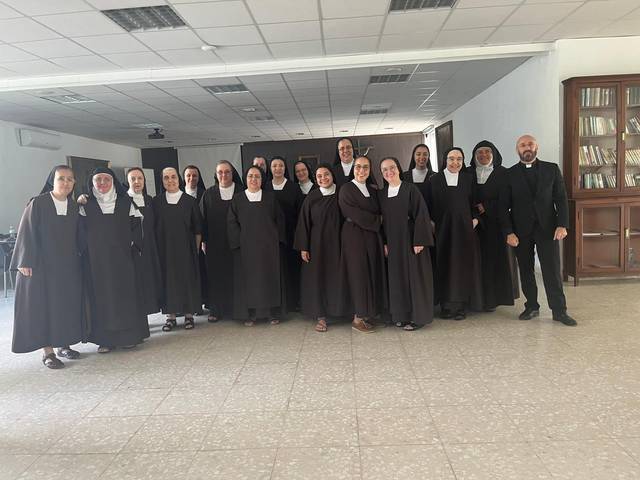 Grupo de monjas y sacerdotes sonriendo para una foto en un salón amplio.