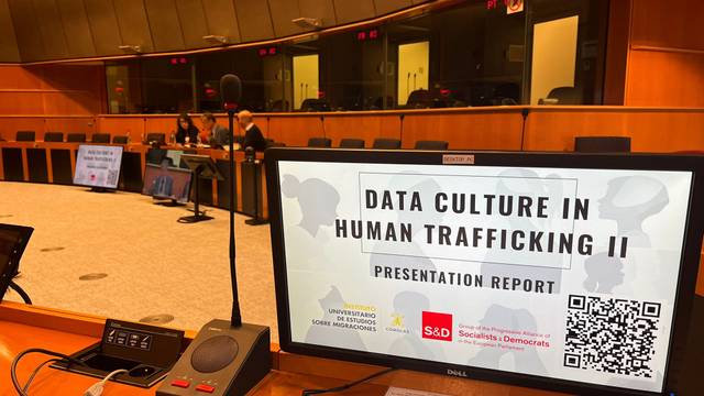 Imagen de una pantalla de presentación en una sala de conferencias mostrando un informe titulado 'Data Culture in Human Trafficking II'.