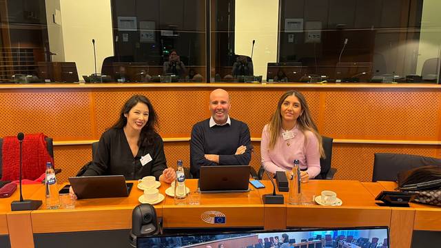 Tres personas sonriendo sentadas en una mesa de conferencia con computadoras portátiles y tazas de café.