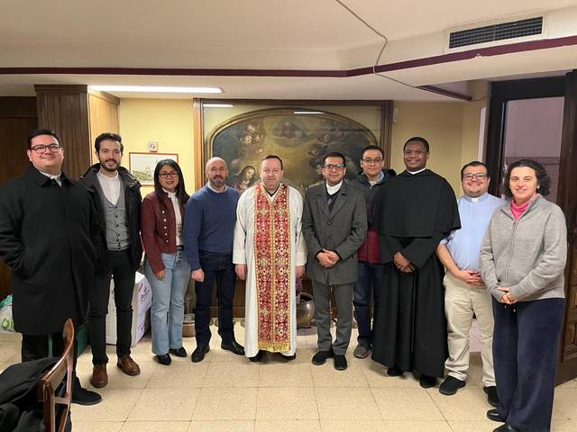 Un grupo de nueve personas, incluyendo un clérigo en vestimentas litúrgicas, posando para una foto dentro de un edificio.