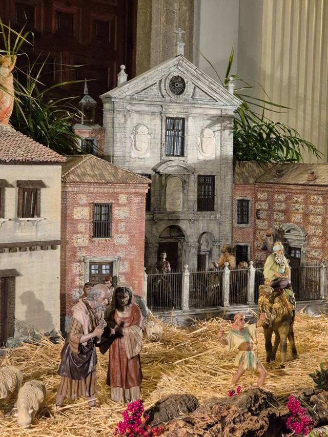 Belén navideño que muestra figuras representando el nacimiento de Jesús con una réplica detallada de un edificio antiguo al fondo.